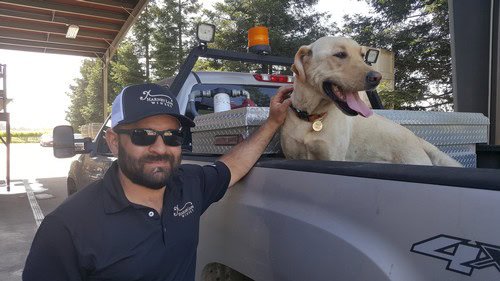 Man and dog at Lodi Winegrape Commission event, enjoying outdoor setting and sunny weather.