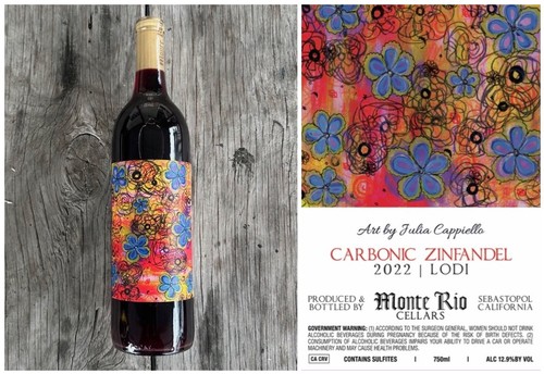 Red wine bottle with colorful label featuring blue flowers and abstract art, on a rustic wooden background.