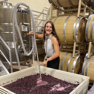 Young woman enjoying wine grape crushing at Lodi Winegrape Commission winery tour.