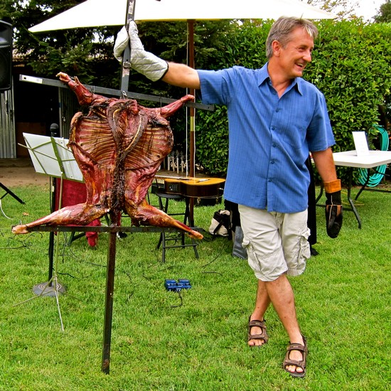 Man holding a roasted pig at a Lodi Winegrape Commission event in a garden setting.