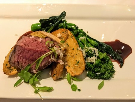 Gourmet beef tenderloin served with roasted potatoes, green beans, broccoli, and a dark sauce on a white plate.