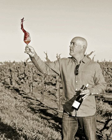 Man holding a wine bottle and a flaming torch in a vineyard, promoting Lodi winegrapes.