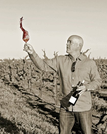 Man holding a wine bottle and tasting a wine in a vineyard, Lodi Winegrape Commission, California.