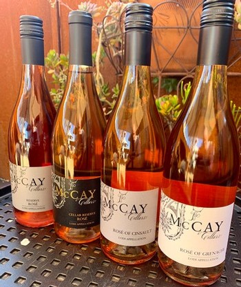 Four bottles of Lodi Winegrape Commission Rosé wine on a black surface with a garden background.