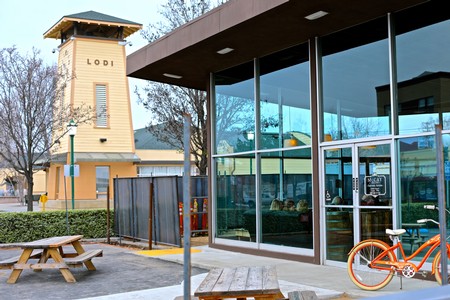 Modern visitor center with glass walls, outdoor seating, and a bike in Lodi, California, promoting local wine tourism.