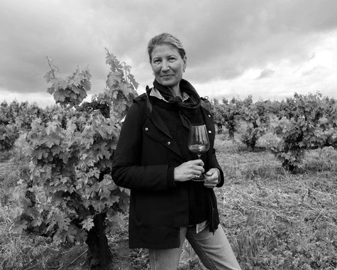 Woman holding a glass of red wine in a vineyard during daytime, with cloudy sky in the background.