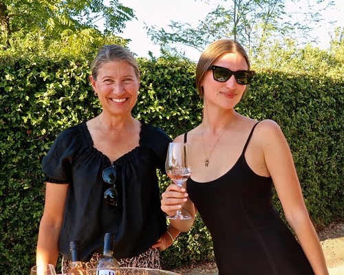 Two women enjoying wine outdoors at a Lodi Winegrape Commission event, smiling and holding a glass of wine.