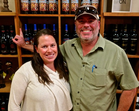 Smiling man and woman at a wine store with wine bottles in the background.