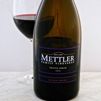 Close-up of Mettler Petite Sirah 2015 wine bottle with glass of red wine in background.
