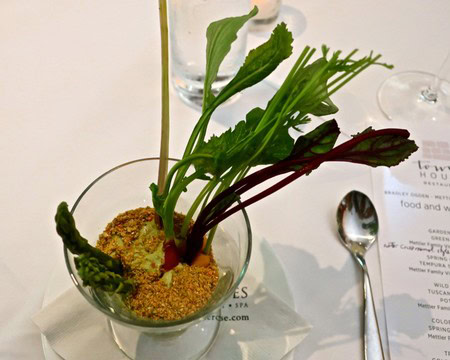 Elegant herb garnish with leafy greens and edible flowers in a glass bowl on a white table.