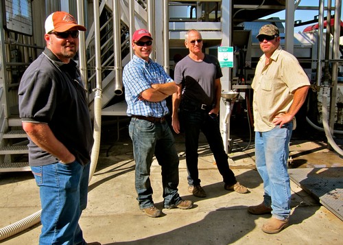 Group of four men standing outdoors at a winery, smiling and posing for the photo.