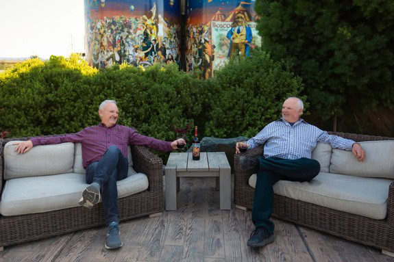 Two men enjoying wine at an outdoor event with Lodi Winegrape Commission mural in background.