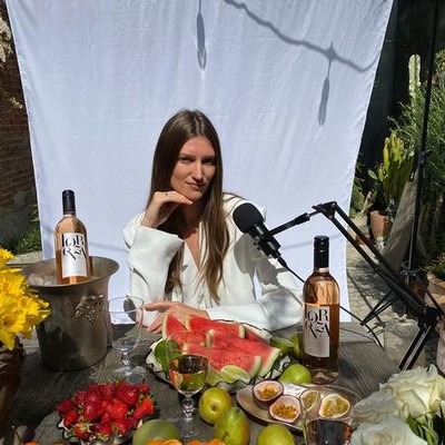 Woman at Lodi Winegrape Commission event with wine bottles, watermelon, and fruits on table.