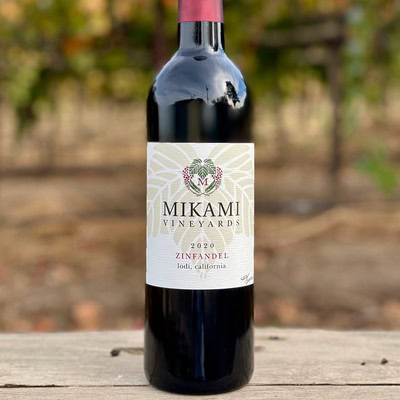 Bottle of Mikami Vineyards Zinfandel 2020 from Lodi, California, on a wooden surface with vineyard background.