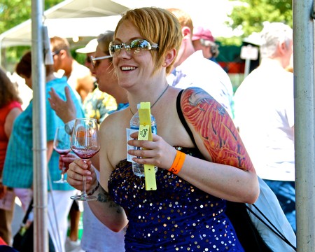 Woman enjoying wine at Lodi Winegrape Commission outdoor event with crowd in background.