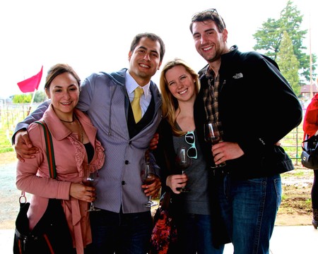 Group of four smiling people at a wine tasting event, holding glasses of wine outdoors.