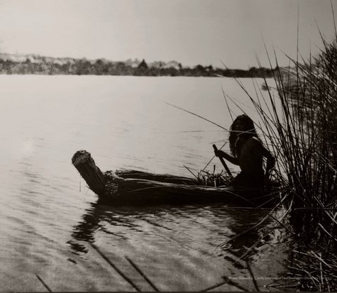 Silhouette of a person fishing from a small boat near the riverbank in Lodi, California.