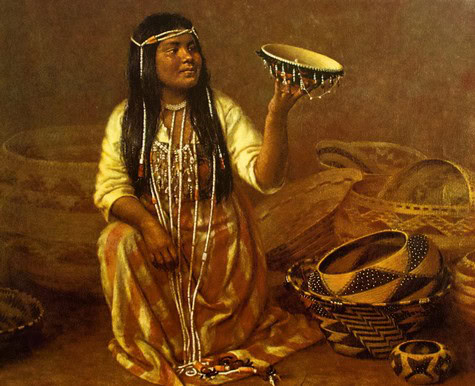 Native woman in traditional attire holding a decorated drum, surrounded by woven baskets and artifacts.