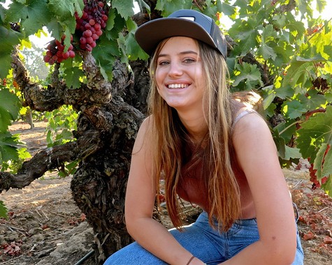 Young woman smiling in a vineyard with grapevines and ripe grapes in the background.