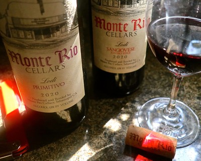 Two bottles of Lodi wine from Monte Rio Cellars with a glass of red wine on a table.