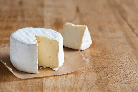 Close-up of soft cheese with a slice cut out, on a rustic wooden table.