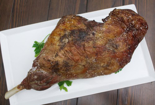 Juicy roasted lamb shank served on a white platter with fresh herbs, perfect for wine pairing in Lodi wine region.