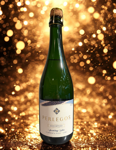 A green bottle of Perlegos Assyrtiko sparkling wine with a cork, against a festive golden bokeh background.