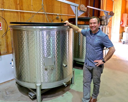 Man standing next to large stainless steel wine fermentation tank at Lodi Winegrape Commission facility.