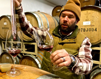 Man tasting red wine in a winery with barrels in the background.