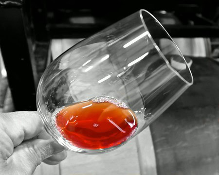Close-up of a hand holding a wine glass with red wine, focus on the glass, black and white background.