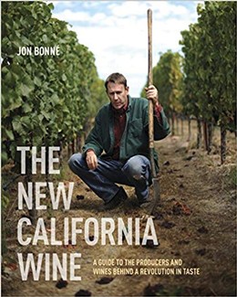 Man kneeling in a vineyard holding a tool, with lush grapevines behind him, promoting California wine.