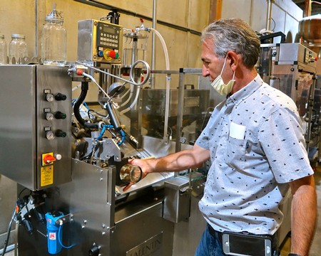 Man operating wine bottling machine in a winery, wearing a face mask and casual shirt.