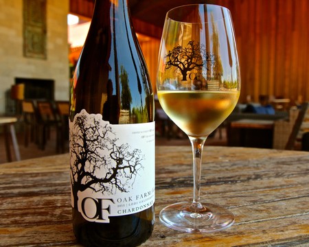 Bottle of Lodi Chardonnay wine with a glass of wine on a rustic table in a winery setting.