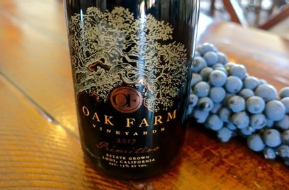 Close-up of Oak Farm Vineyard wine bottle with grapes in the background.