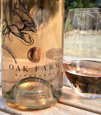 Lodi Winegrape Commission wine bottle and glass of rosé wine outdoors.