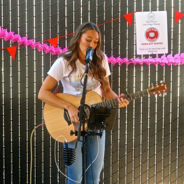 Young woman playing guitar and singing at Lodi Winegrape Commission event with festive decorations.