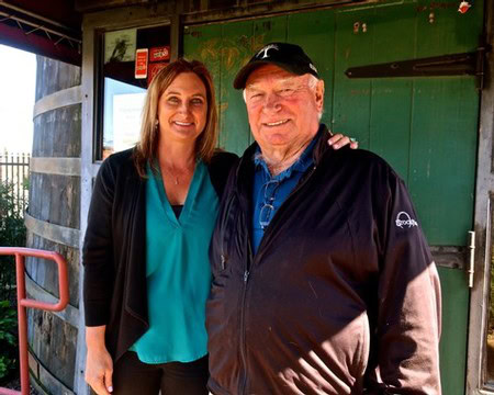 Two smiling individuals at a Lodi Winegrape Commission event, outdoors with a rustic background.