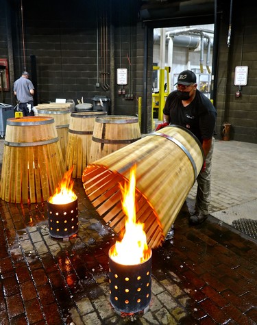 Worker inspecting a large wooden wine barrel in a winery workshop with fire pits nearby.
