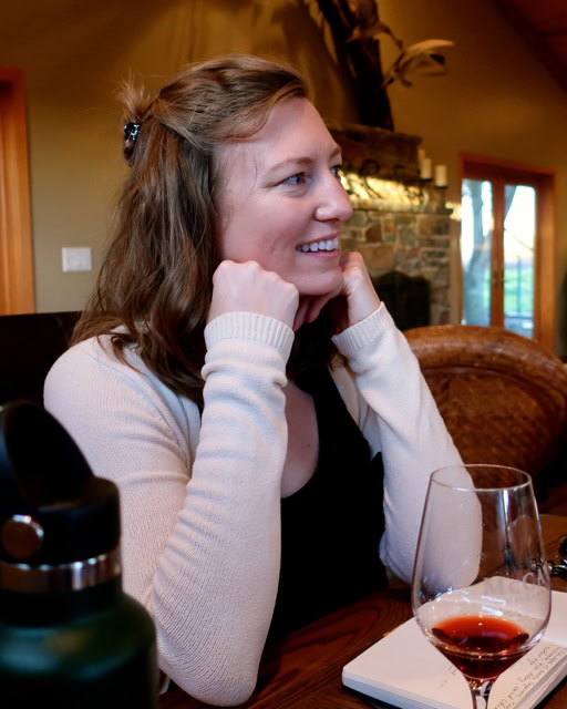 Woman smiling and enjoying a glass of red wine at a cozy winery setting.