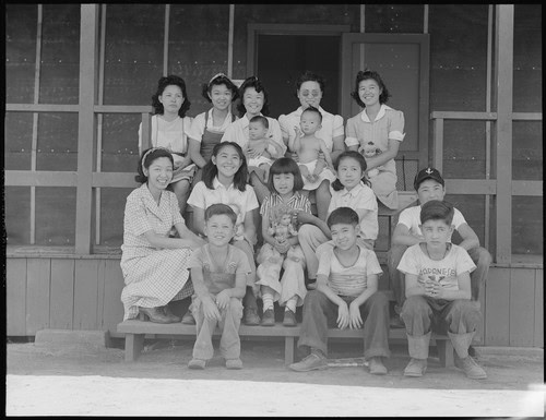 Black and white photo of children and women sitting on steps outside a building.
