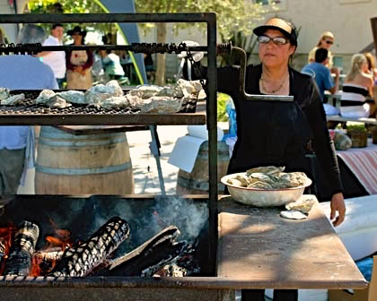 Woman grilling oysters at Lodi Winegrape Commission outdoor event with guests in background.