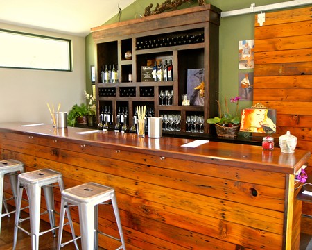 Interior of a wine tasting room with a wooden bar, wine bottles, glasses, and decorative plants.