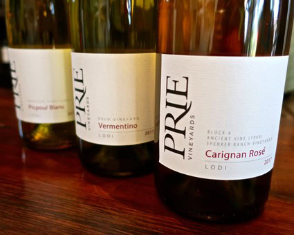 Close-up of Lodi Winegrape Commission wine bottles, including Vermentino and Carignan Rosé, on a wooden surface.