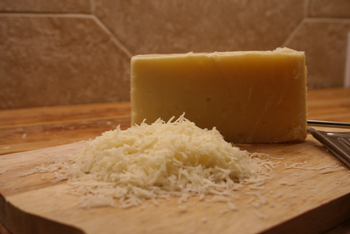 Close-up of a block of hard cheese with grated cheese on a wooden cutting board.