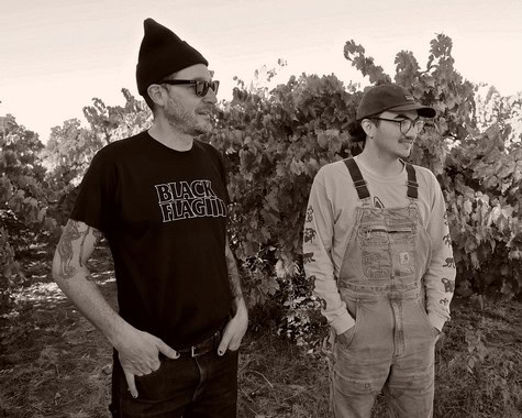 Two people standing in a vineyard, smiling, with grapevines in the background, representing Lodi Winegrape Commission.