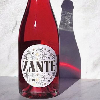 Zante sparkling wine bottle with a white label and black text, casting a shadow on a white surface.