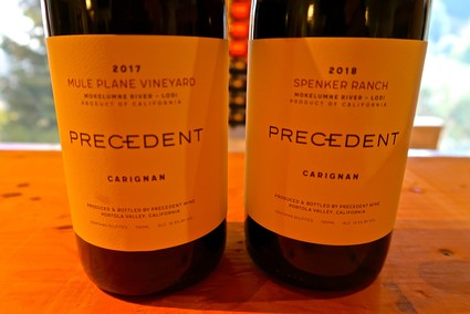 Two bottles of wine from Lodi Winegrape Commission, 2017 and 2018, on a wooden surface with a blurred outdoor background.
