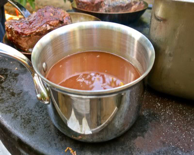 Close-up of a stainless steel cup filled with red wine, surrounded by wine-making tools and grapes.