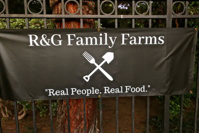 R&G Family Farms sign on a fence with the slogan "Real People. Real Food.".
