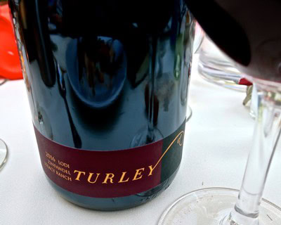 Close-up of a dark wine bottle with a red and gold label reading 'Turley' at a wine tasting event.